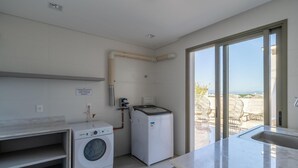 A modern laundry room with a washing machine, dryer, and a large window offering a view of outdoor wicker furniture. - Ap in a Condominium With gym in Jurere Vox0210 (Florianópolis)