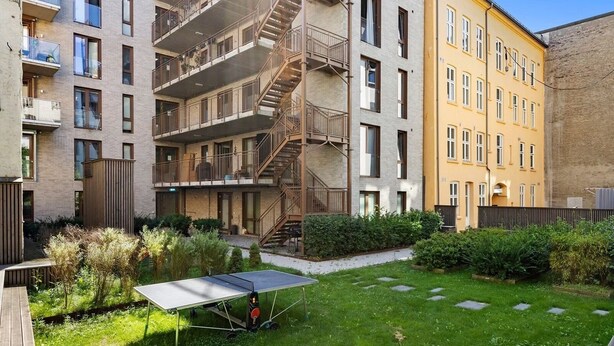 Un immeuble résidentiel à plusieurs étages, doté de balcons, d’un panneau solaire et d’un jardin bien entretenu.