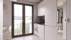 Une cuisine moderne avec des meubles blancs, un plan de travail noir et une grande porte-fenêtre coulissante donnant sur un balcon.