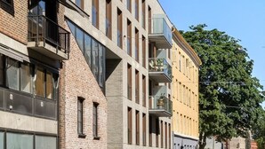 Un immeuble à plusieurs étages dont la façade combine des éléments en brique et un style moderne, avec des balcons ornés de jardinières et de grandes fenêtres.
