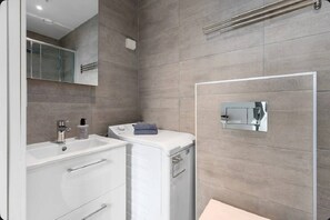 A modern bathroom with a large mirror, a sink, a washing machine, and a shower area. - Quiet Studio in Oslo Center Queen Bed & Rooftop (Oslo)