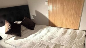 Un lit avec un matelas blanc et une tête de lit sombre.