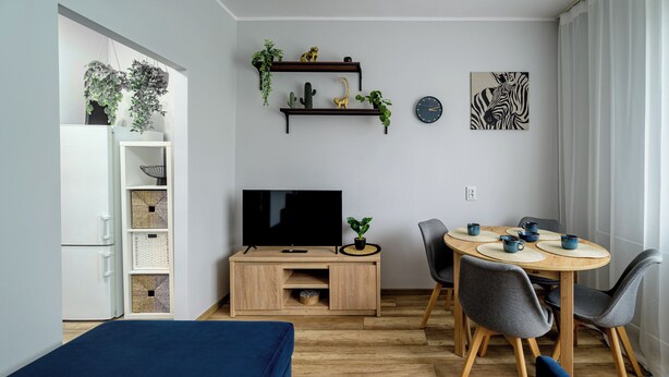A modern living room with a TV, dining table, chairs, and a sofa. - RentPlanet - Apartament Zdrowa (Wrocław)