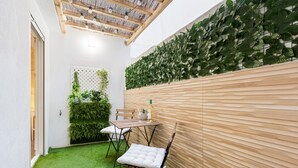 Un patio con una mesa y sillas de madera, piso de césped artificial verde y una pared cubierta de follaje verde.