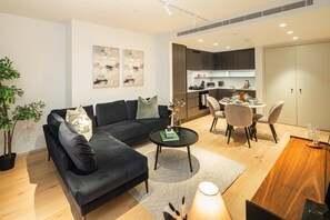 Ein modernes Wohnzimmer mit einem schwarzen Sofa, einem runden Couchtisch und einem Essbereich mit Tisch und Stühlen.