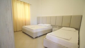A hotel room with two beds, a bedside table, and a curtain. - Hostel K13 (Sarande)