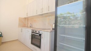 A compact kitchen with white cabinets, a built-in oven, and a glass-fronted refrigerator. - Hostel K13 (Sarande)