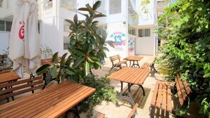 An outdoor seating area with wooden tables and benches, surrounded by greenery and white walls. - Hostel K13 (Sarande)