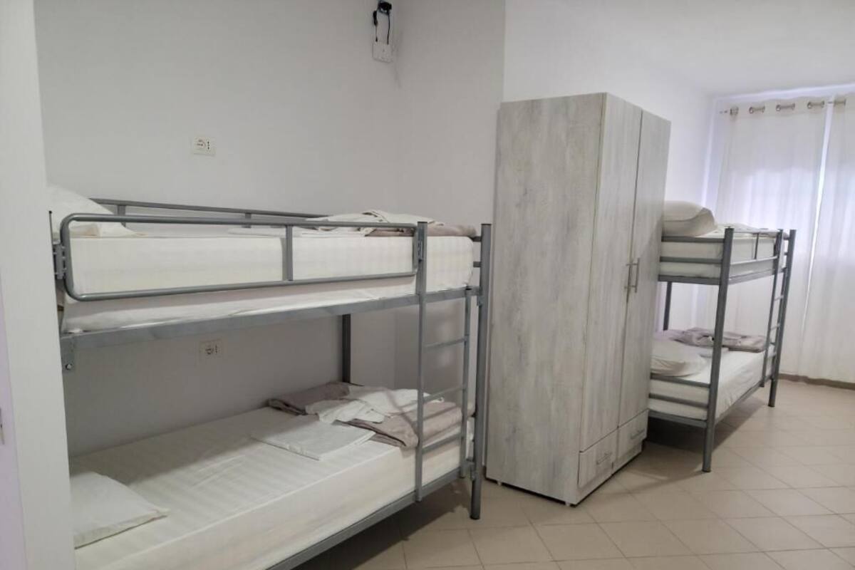 A dormitory room with bunk beds, a wardrobe, and a window with curtains.