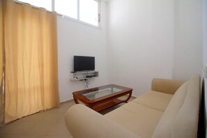 A living room with a sofa, a glass-top coffee table, a television on a shelf, and a window with curtains. - Hostel K13 (Sarande)
