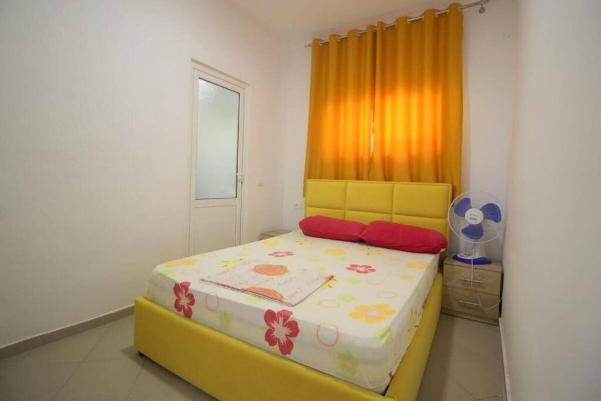 A bedroom with a bed, a nightstand, a fan, and a window with curtains.