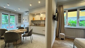 A modern kitchen with a dining area, a TV mounted on the wall, and a view of greenery outside. - Deluxe Apartment - Vespucci (stresa)