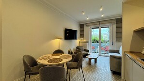 Una sala de estar moderna con una mesa redonda, sillones grises, un sofá, un televisor montado en la pared y un ventanal corredero que da a un espacio exterior con sillas.
