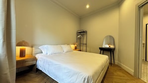 Un dormitorio ordenado con cama, lámparas de noche, mesitas de noche, un espejo y un perchero.