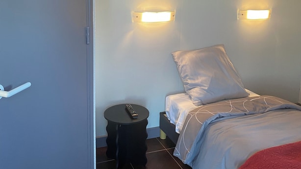 A bedroom with a bed, two wall-mounted lights, a round nightstand, a remote control, and a door. - fasthotel troyes  (Barberey-Saint-Sulpice)