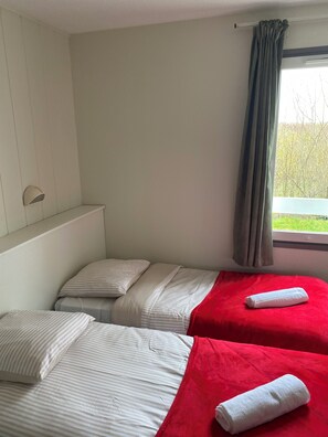A hotel room with two beds, a window with curtains, a small shelf, and a view of greenery outside. - fasthotel troyes  (Barberey-Saint-Sulpice)