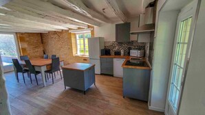 A compact kitchen with a dining area, stone walls, and a view of greenery outside. - Charming cottage Les Prés (Saint-Cyprien)