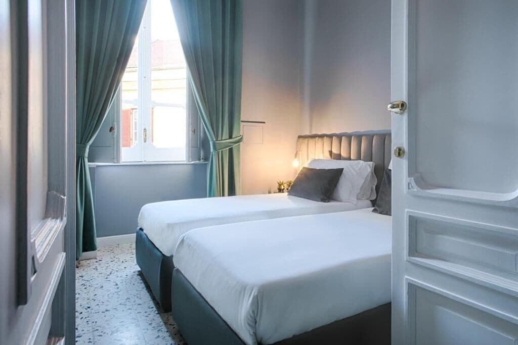 Un dormitorio con dos camas, una ventana con cortinas, un radiador y una puerta.