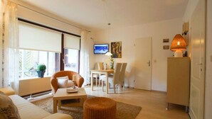 A living room with a sofa, a dining table with chairs, a television, and a lamp. - Apartment 2 - Holiday home Sternmöwe Cuxhaven (Cuxhaven)