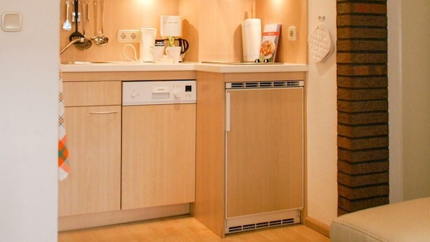 A compact kitchen with wooden cabinets, a microwave, a coffee maker, and a dishwasher. - Apartment 2 - Holiday home Sternmöwe Cuxhaven (Cuxhaven)