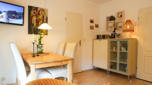 A dining area with a wooden table and white chairs, a cabinet with glass doors, and a television mounted on the wall. - Apartment 2 - Holiday home Sternmöwe Cuxhaven (Cuxhaven)