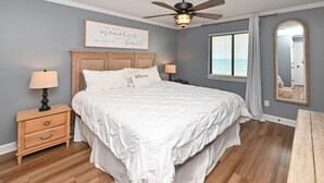 A bedroom with a large bed, wooden headboard, two bedside tables with lamps, a ceiling fan, and a window with blinds. - Oceanfront 2 BR Condo with Shared Pool! - Surfwatch II 304  - The Family Dream (Surfside Beach)