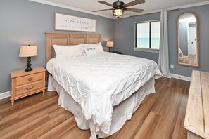 A bedroom with a large bed, wooden headboard, two bedside tables with lamps, a ceiling fan, and a window with blinds. - Oceanfront 2 BR Condo with Shared Pool! - Surfwatch II 304  - The Family Dream (Surfside Beach)