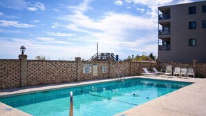 A rectangular swimming pool with clear blue water, surrounded by a brick wall and a building with balconies. - Oceanfront 2 BR Condo with Shared Pool! - Surfwatch II 304  - The Family Dream (Surfside Beach)