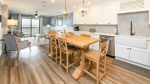A spacious kitchen with a wooden dining table and chairs, white cabinets, and a view to the outside. - Oceanfront 2 BR Condo with Shared Pool! - Surfwatch II 304  - The Family Dream (Surfside Beach)