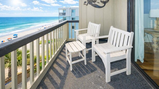 A balcony with white chairs and a small table, overlooking a beach with umbrellas and a building in the background. - Oceanfront 2 BR Condo with Shared Pool! - Surfwatch II 304  - The Family Dream (Surfside Beach)