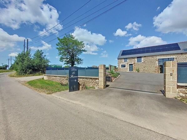 Un bâtiment en pierre avec une entrée pavée, un panneau indiquant une direction et des panneaux solaires sur le toit.