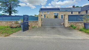 A stone building with a paved entrance, solar panels on the roof, and a sign indicating a direction. - Gîte du Fresne, 30min Mt Saint Michel, 15 min Fougères, 13pers+, sauna, jacuzzi (Les Portes du Coglais)