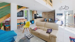 A spacious living area with a sofa, a coffee table, and a dining table. There is a kitchen area with a stone wall and a balcony with a bicycle. - Gîte du Fresne, 30min Mt Saint Michel, 15 min Fougères, 13pers+, sauna, jacuzzi (Les Portes du Coglais)