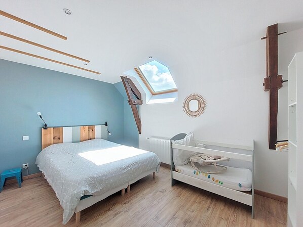 Une chambre à coucher avec un lit, une commode blanche, un petit bureau et une lucarne.