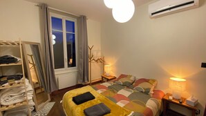 A bedroom with a bed, a bedside table with a lamp, a wardrobe, a window with curtains, and an air conditioner on the wall.