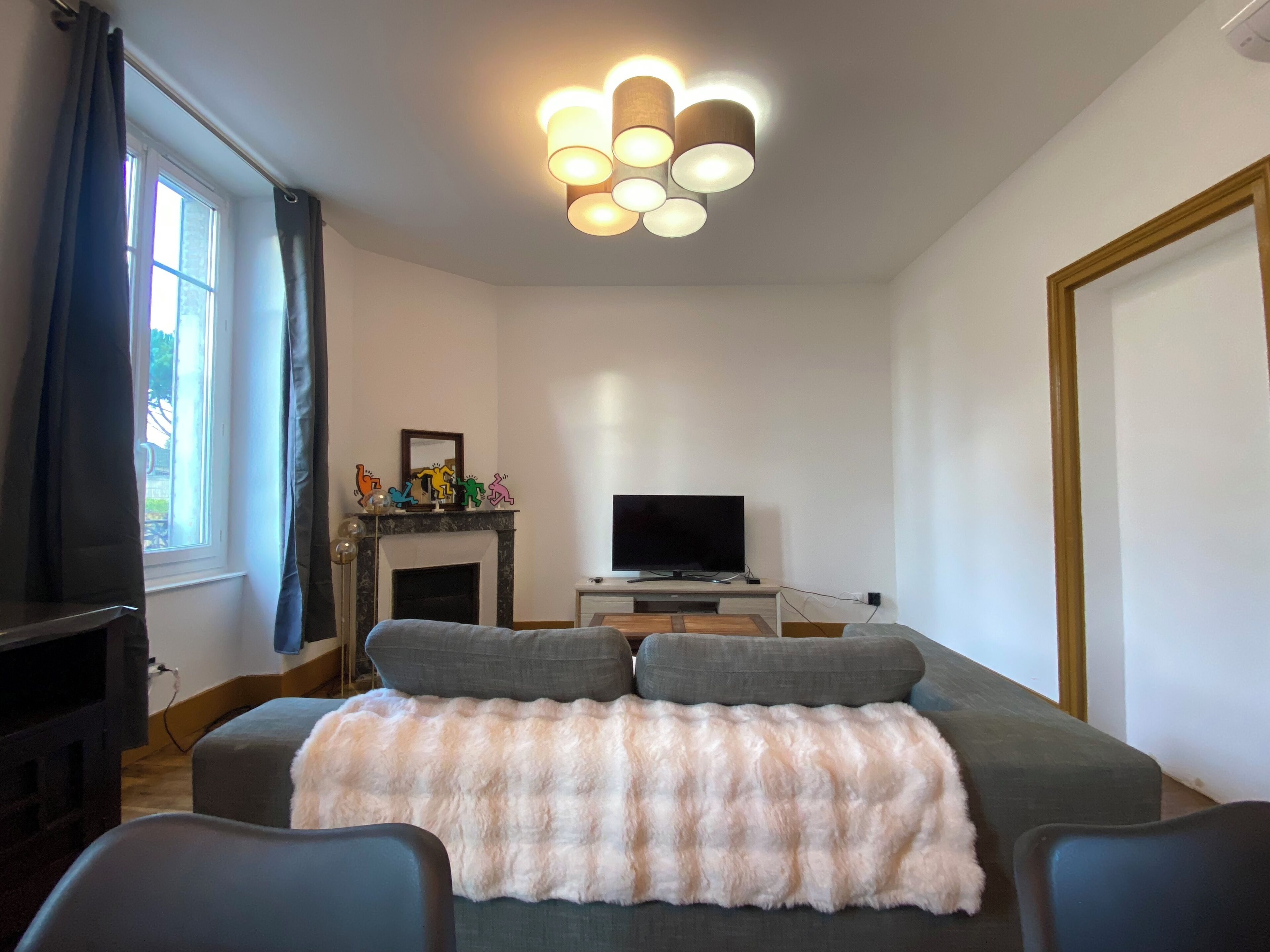 A modern living room with a sofa, a flat-screen TV, a fireplace, and a ceiling light fixture.