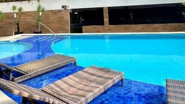 Un edificio moderno con varios balcones y una piscina con sillones de descanso.