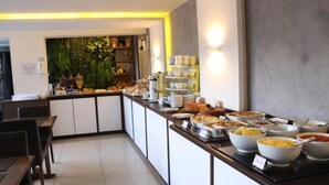 Un bufé con diversos alimentos, una zona de estar con mesas y sillas, y una pared decorativa con plantas.