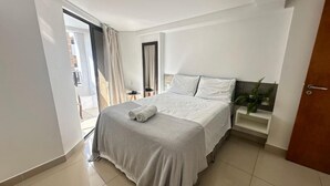 Habitación de hotel moderna con una cama grande, una mesita de noche pequeña y vistas al exterior.