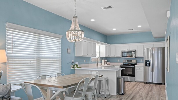 A modern kitchen with white cabinets, stainless steel appliances, and a wooden dining table with white chairs. - Private pool - 2nd tier - Entire Duplex (Gulf Shores)