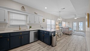 A modern kitchen with dark blue cabinets, a white countertop, and a built-in dishwasher. There is a dining area with a table and chairs, and a ceiling fan above. - Private pool - 2nd tier - Entire Duplex (Gulf Shores)