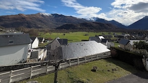 Ein ländliches Dorf mit Häusern, einer grünen Fläche und Bergen im Hintergrund.