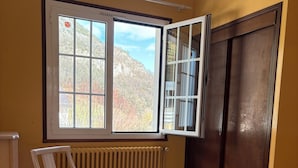 Ein Schlafzimmer mit Bett, Stuhl, Heizkörper und einem Fenster mit Bergblick.
