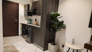 Ett modernt kök med inbyggd mikrovågsugn, ugn och tvättmaskin. Det finns en krukväxt och ett litet bord med en stol.