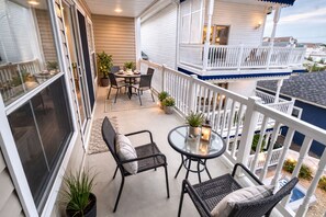 A balcony with a table and chairs, potted plants, and a view of neighboring houses. - Beach Block Sleeps 8 4BR Family Retreat includes bunk beds Walk to Beach (Seaside Heights)