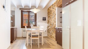 A kitchen with a stone wall, white cabinets, and a dining area with chairs and a table. - CostaBlancaDreams - Casa Paquita in Calpe (Calpe)