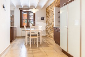 A kitchen with a stone wall, white cabinets, and a dining area with chairs and a table. - CostaBlancaDreams - Casa Paquita in Calpe (Calpe)