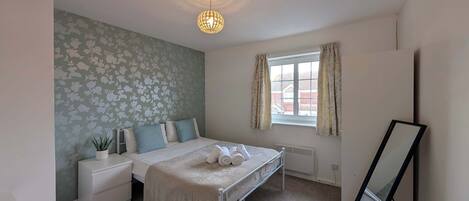 A bedroom with a bed, nightstands, a radiator, a window with curtains, and a mirror.