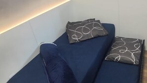 Pieni, moderni huone, jossa on tummansininen sohva, kaksi kuviollista koristetyynyä ja puulattia.