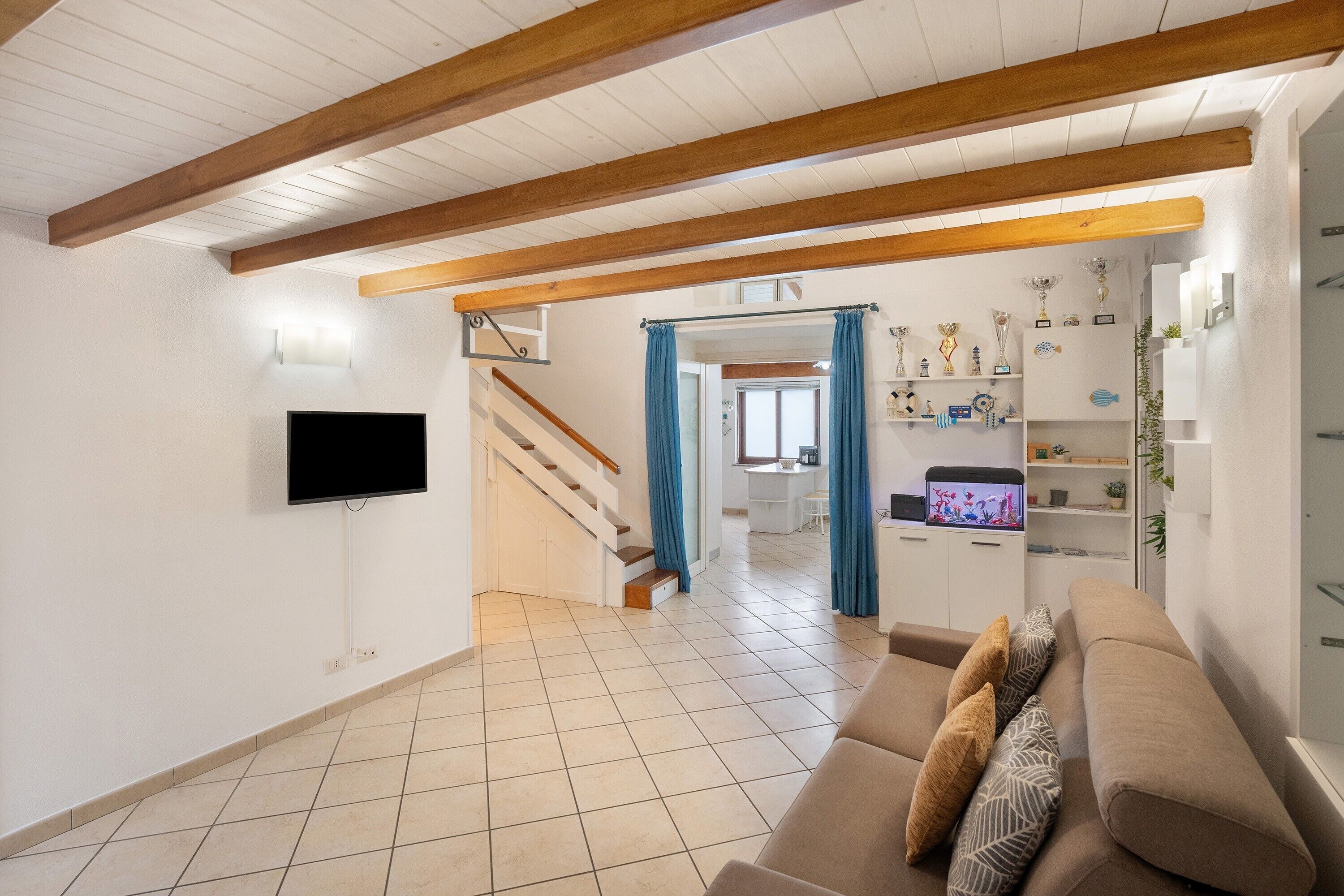 Una sala de estar con sofá, televisión y una escalera que lleva a otra habitación.